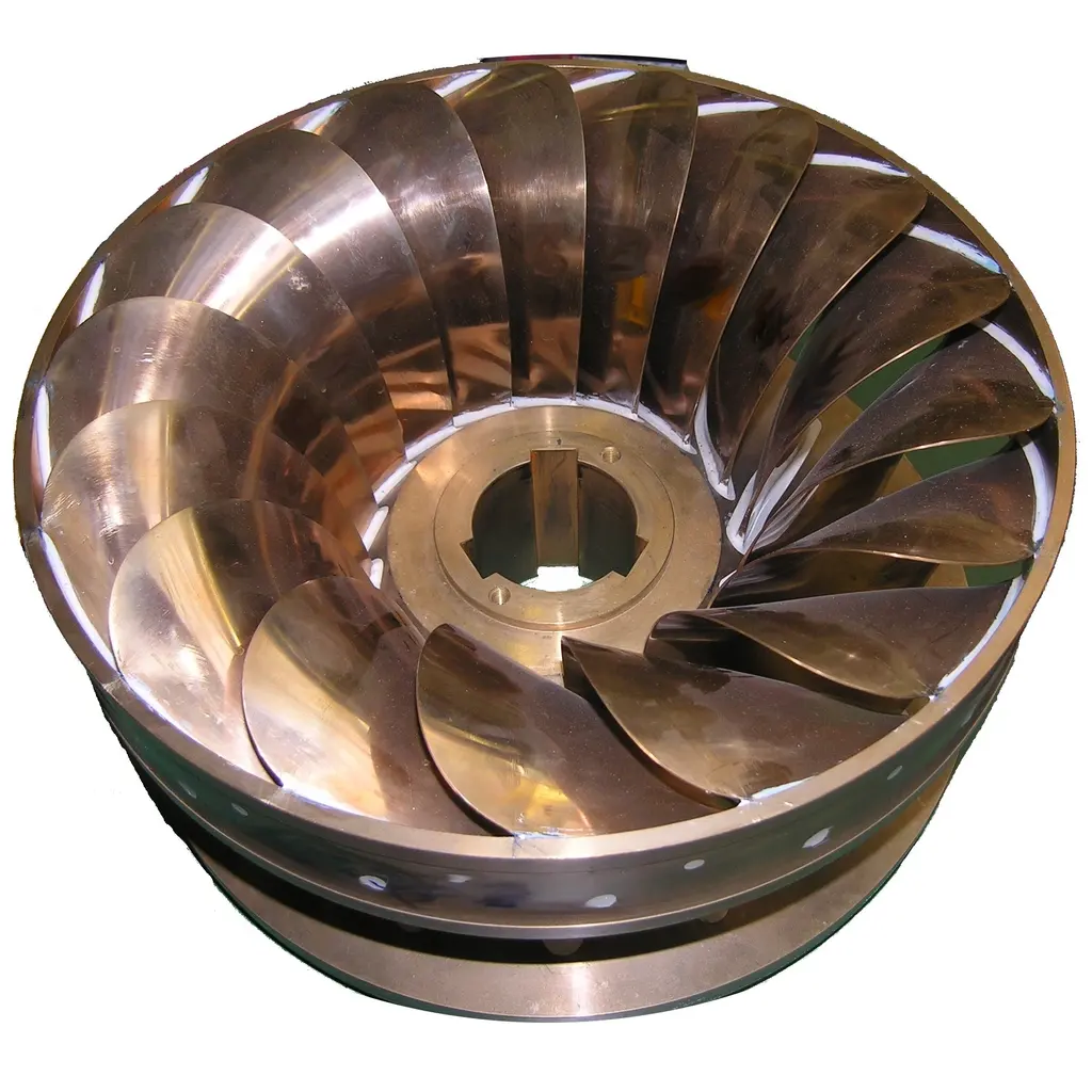 A polished water-turbine rotor with curved metal blades surrounding its central shaft opening.