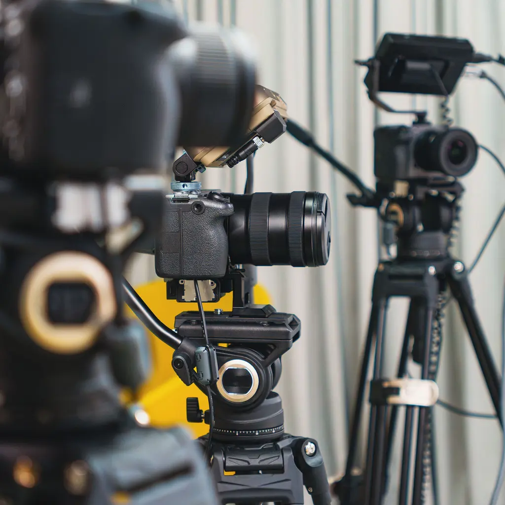 Video cameras with screens and cables stand on tripods in a studio.