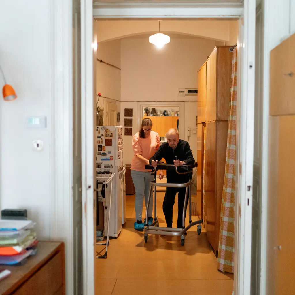 A caregiver supporting an older adult using a walker indoors.