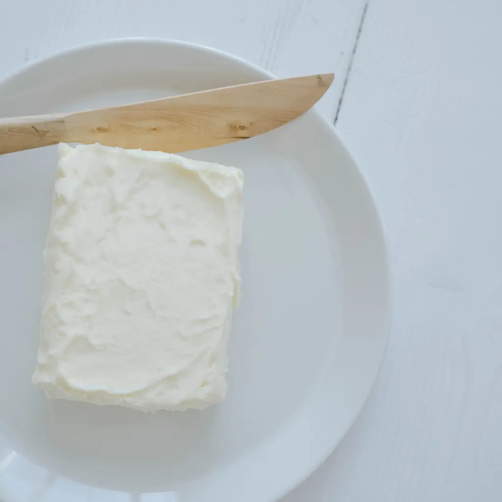 A pale block of butter on a white plate beside a wooden butter knife.