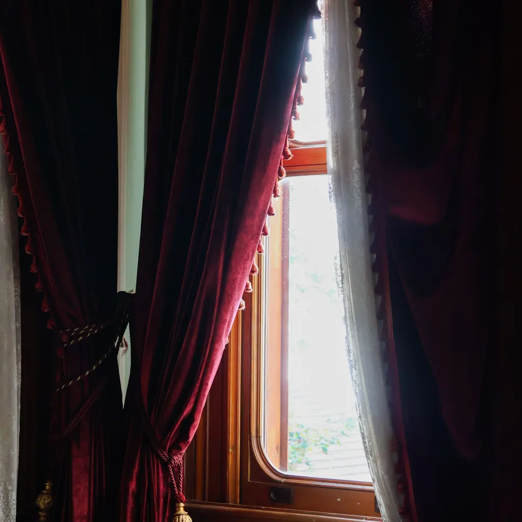 Deep-red drapes tied back around a wooden-framed window.