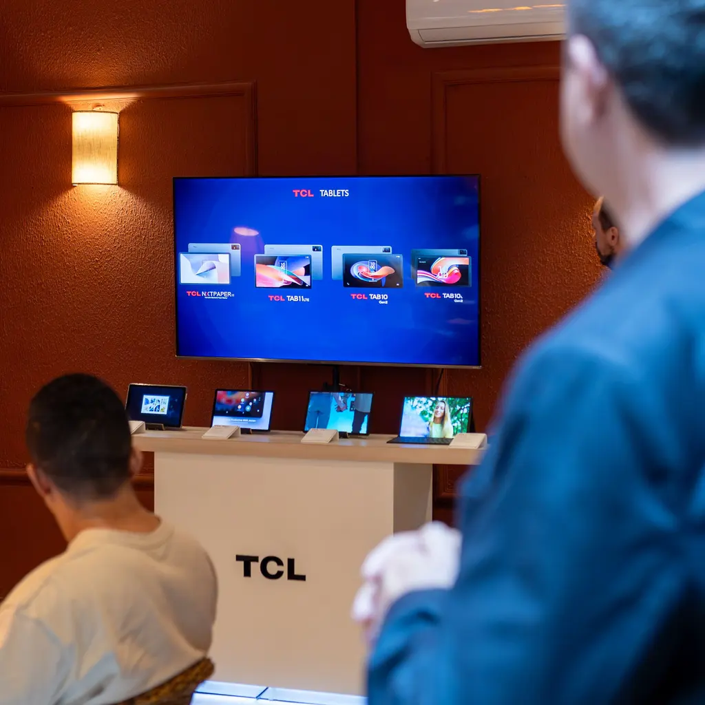 Electronic devices displayed beneath a screen in a technology showroom.