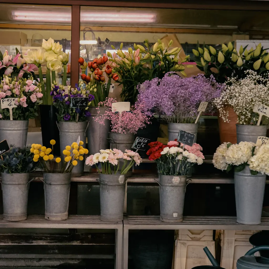 Buckets holding bunches of cut flowers in several colors on tiered shelves.