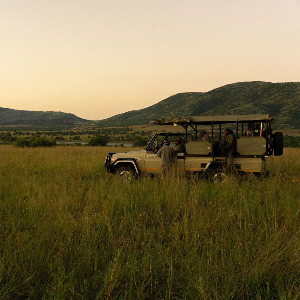 An open safari vehicle and people in grassland within a wildlife reserve.