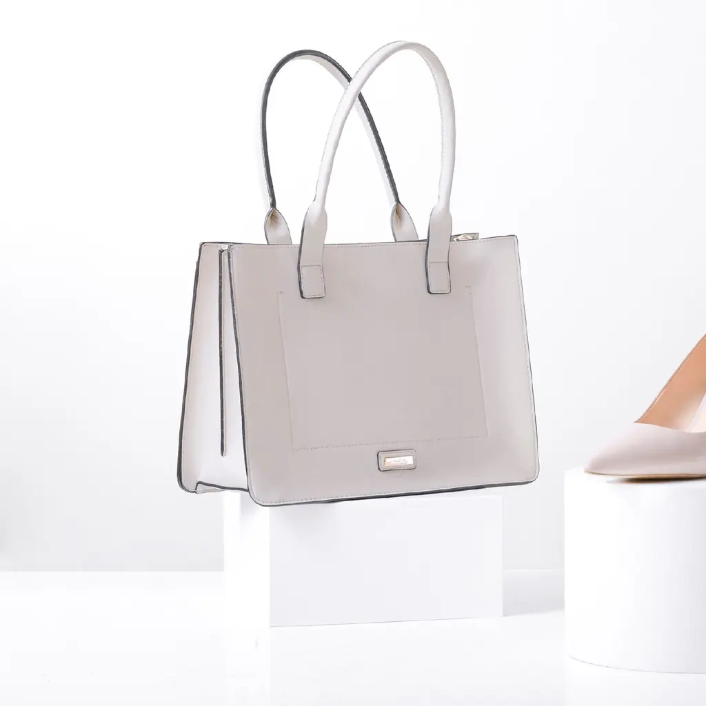 A light-colored leather handbag displayed on a white pedestal.