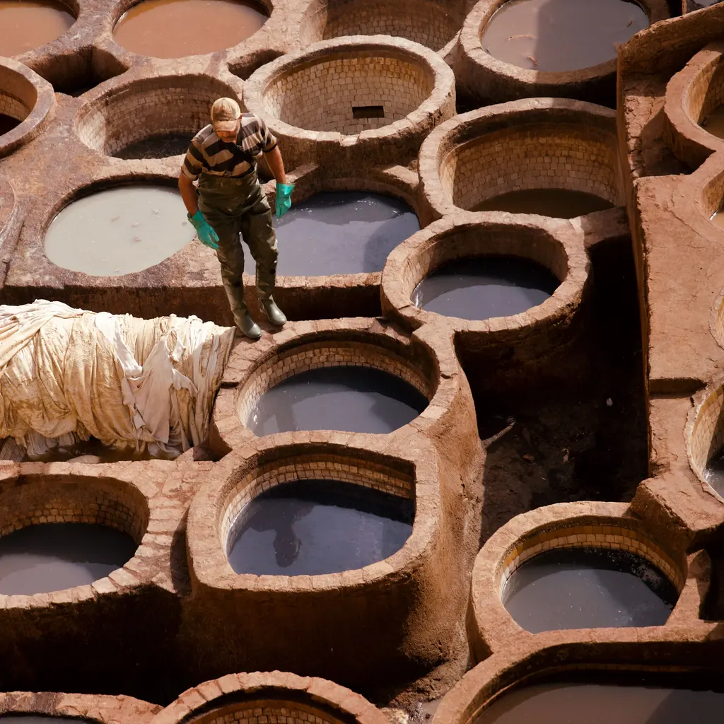 A worker handling a hide among circular leather-tanning vats.