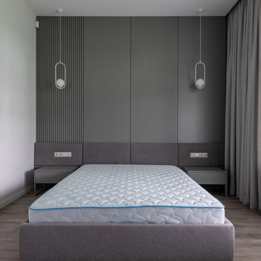 An uncovered quilted mattress on a bed frame in a gray room.