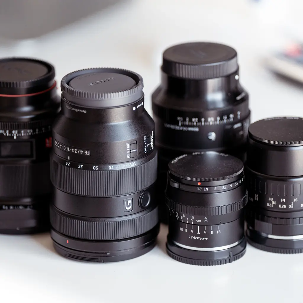 An assortment of interchangeable camera lenses arranged on a white surface.