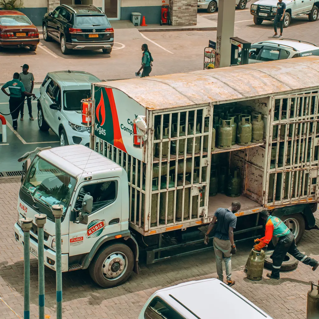An LPG delivery truck carrying gas cylinders, with workers alongside it.