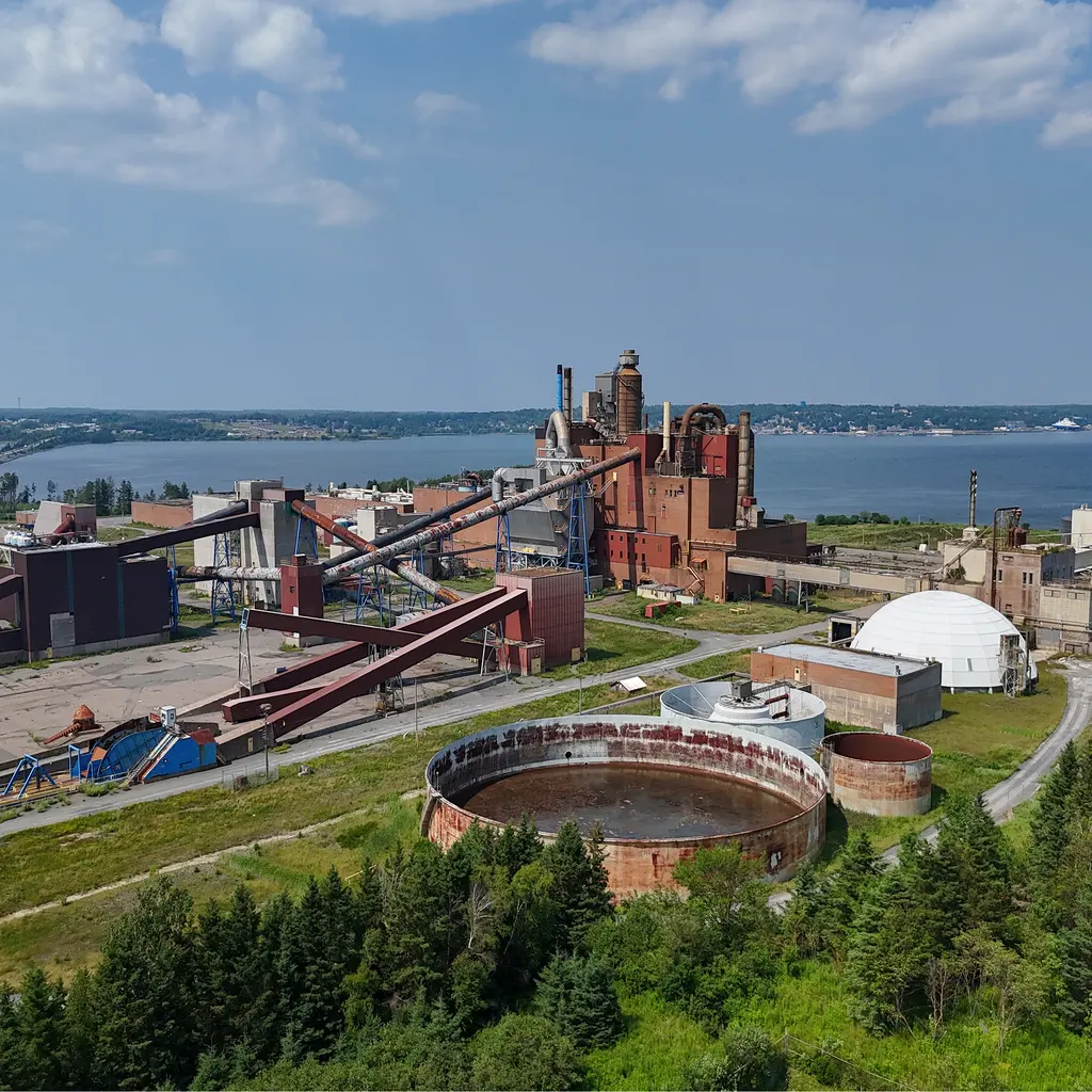 Pulp-mill buildings and enclosed conveyors beside large circular process tanks.