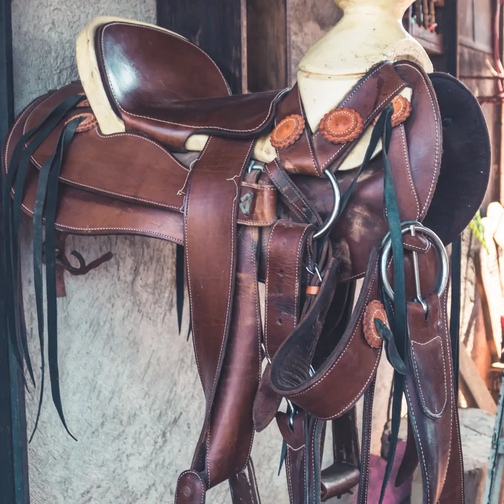 A tooled brown leather riding saddle with stirrups and straps hanging from a wall.