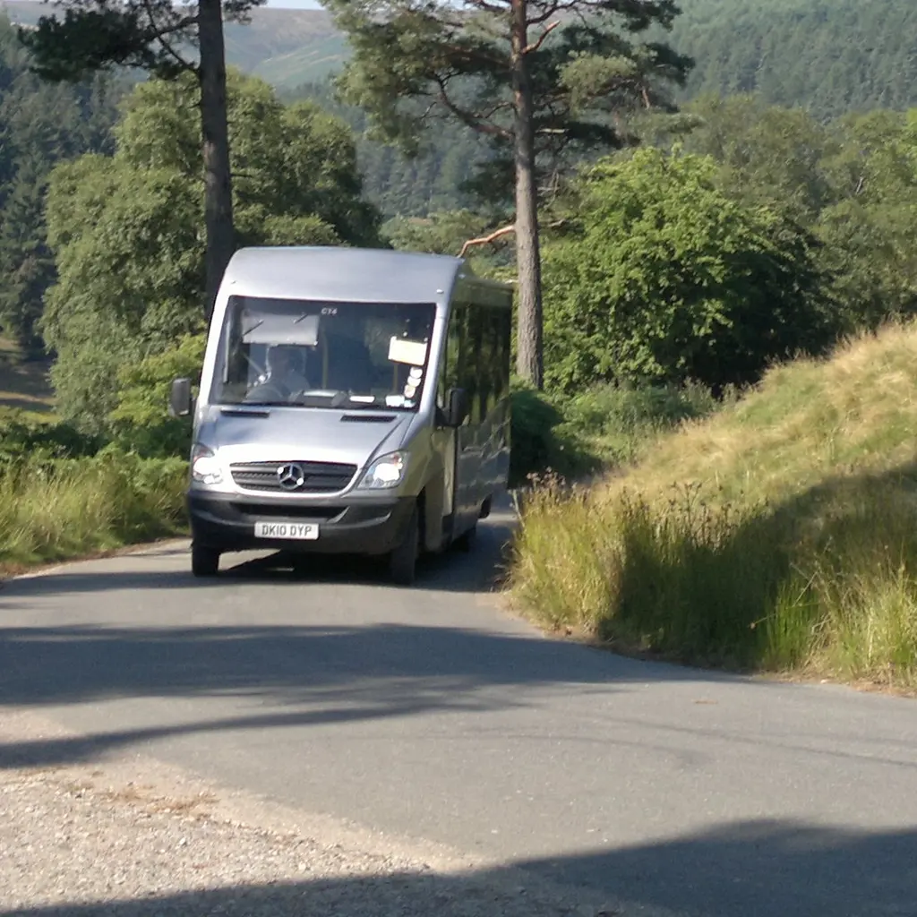 A small passenger shuttle traveling along a wooded road.