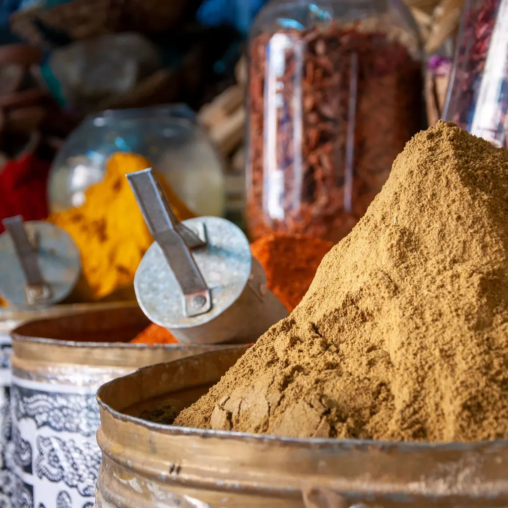 Mounds of powdered spices in metal containers with small scoops.