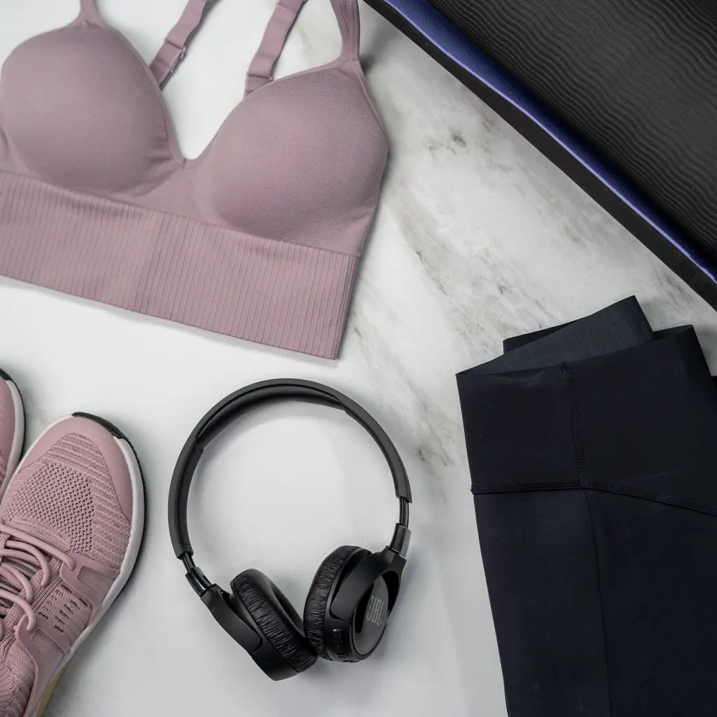 A sports bra and leggings arranged beside exercise shoes and headphones.