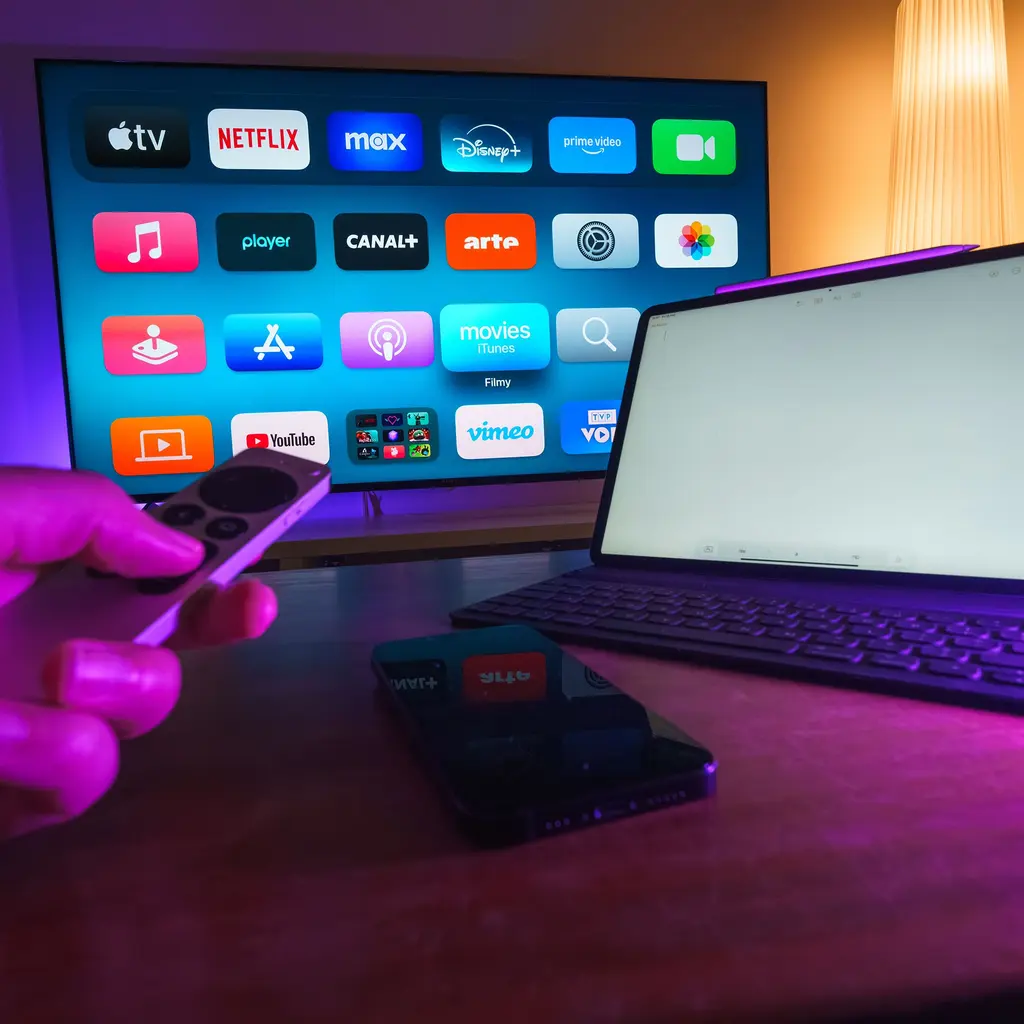 A television displaying streaming-service apps beside a laptop, phone and remote control.