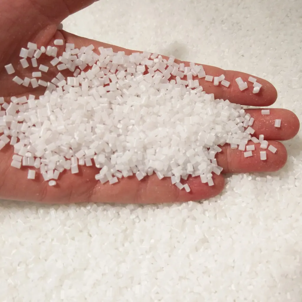 White plastic resin pellets resting in an open hand above more pellets.