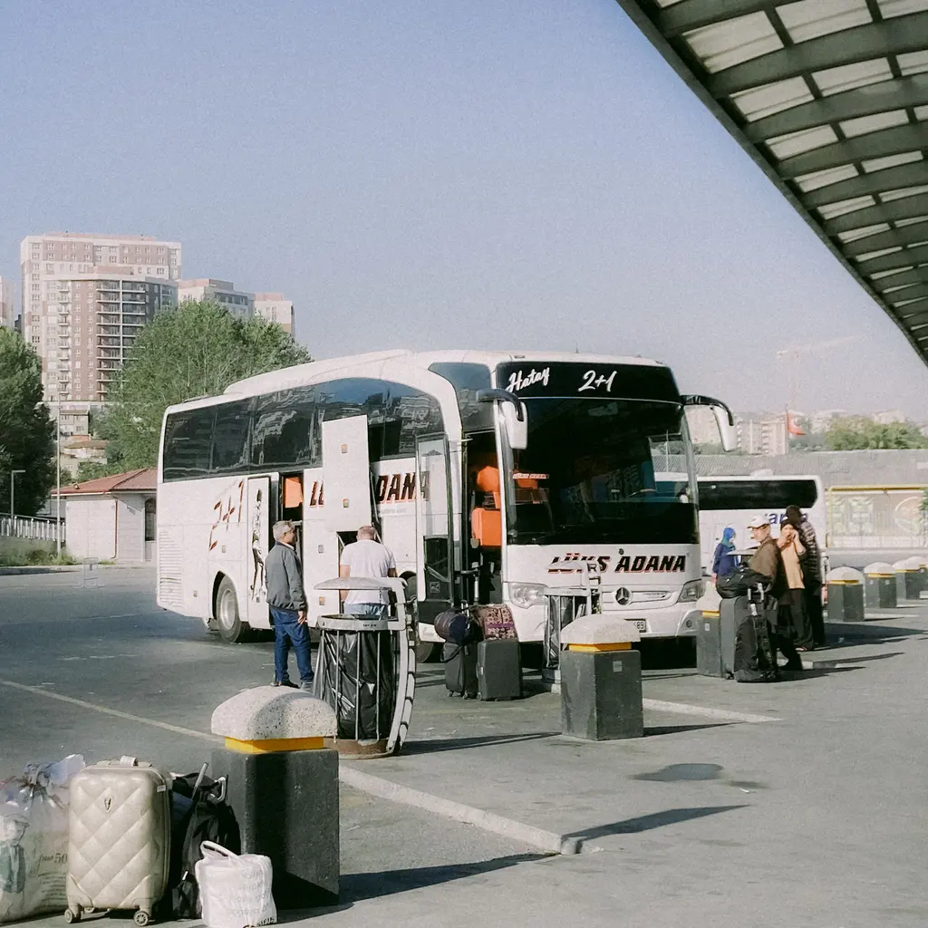 A passenger coach and travelers with luggage at a bus station.
