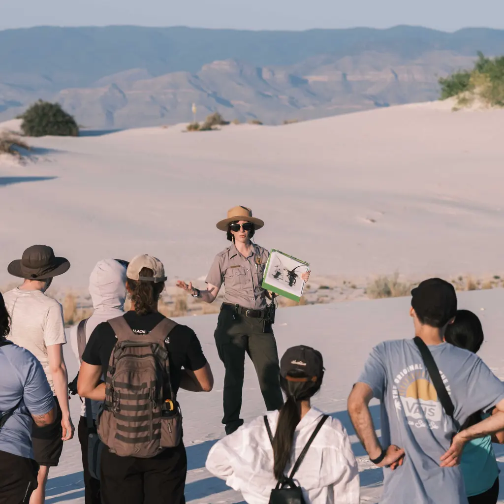 A guide speaking to a group of visitors on a sandy outdoor tour.