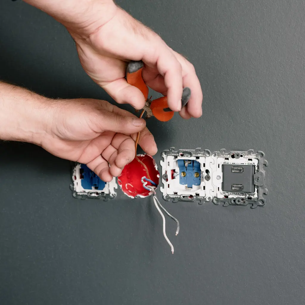 Hands connecting wiring to electrical socket and switch mechanisms set into a wall.