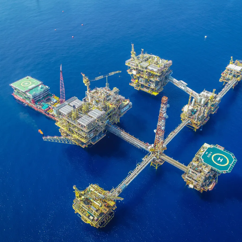 An offshore oil-platform complex has connected decks, cranes and helipads above blue water.