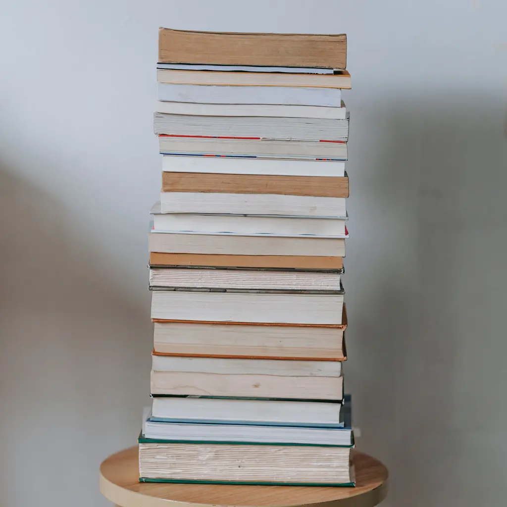 A tall stack of paperback and hardcover books with their page edges facing outward.