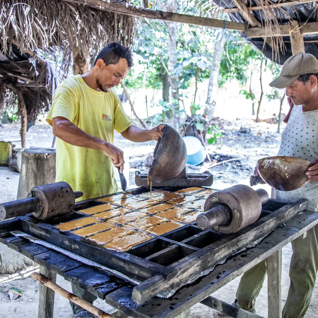 Workers pouring hot cane-sugar mixture into molds during panela production.
