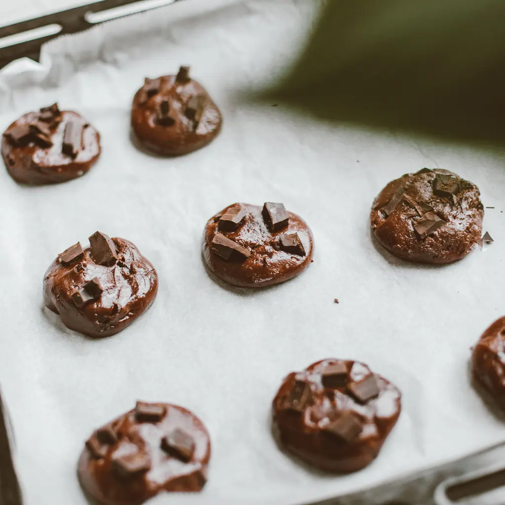 Chocolate cookie dough portions arranged on a lined baking sheet.
