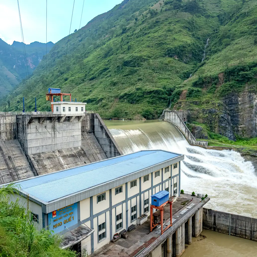Water flows over the spillway of a concrete dam beside its power station.