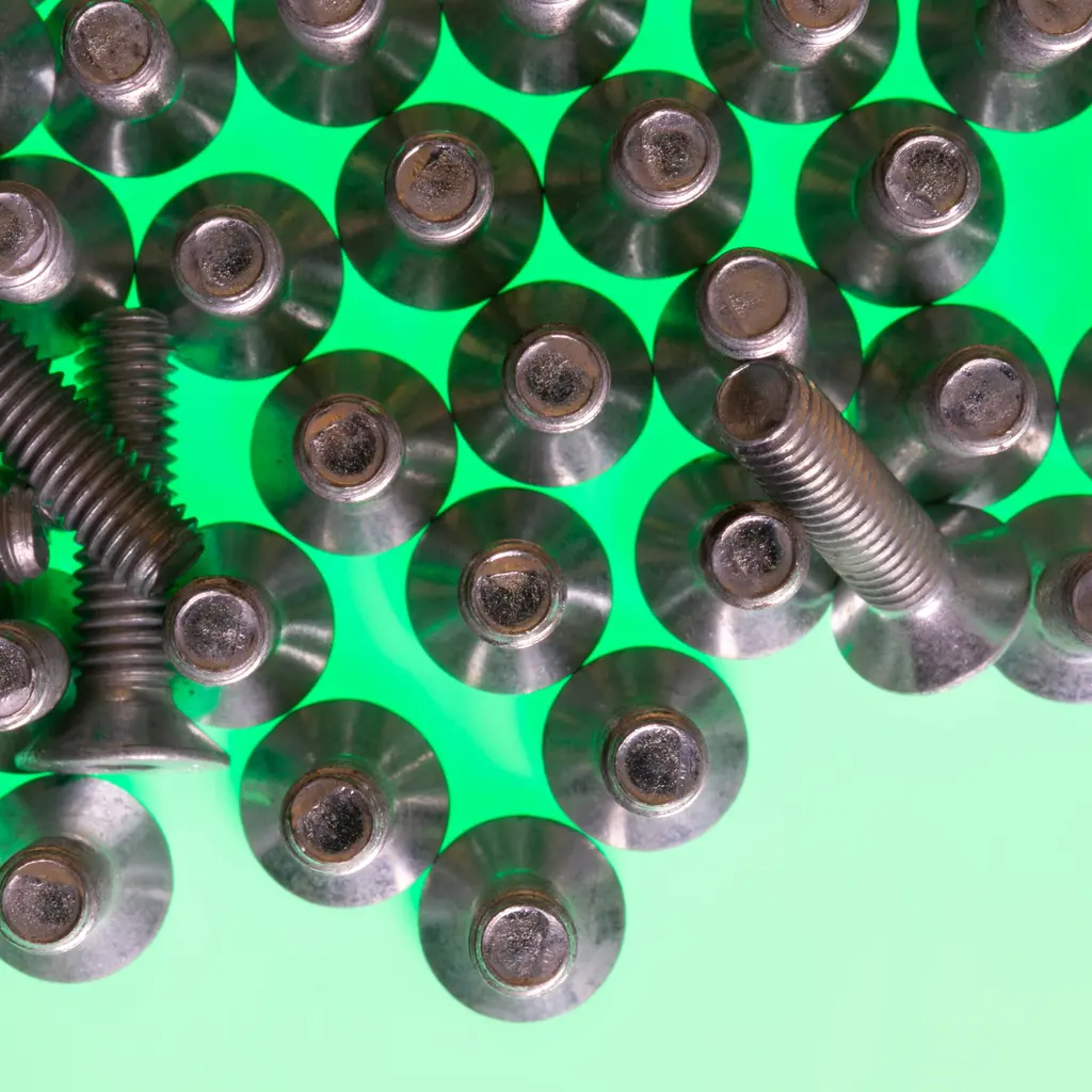 Metal socket-head screws and fasteners arranged on a green surface.
