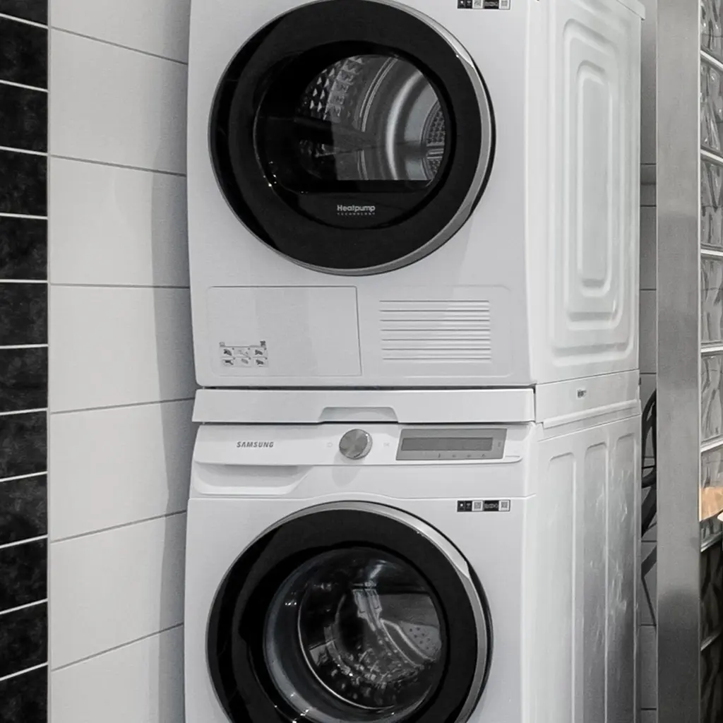 A stacked front-loading clothes dryer and washing machine against a tiled wall.