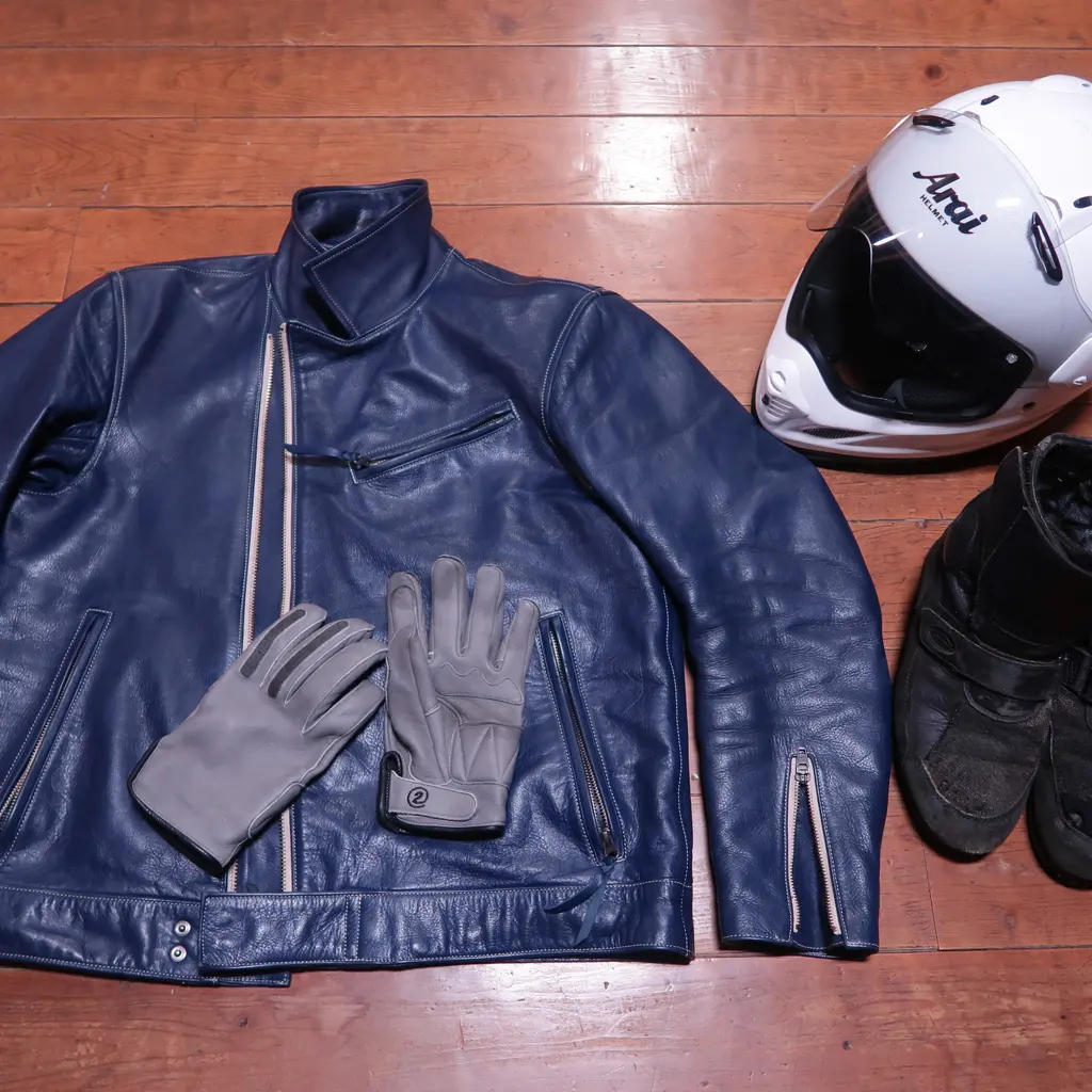 A leather motorcycle jacket, protective gloves, riding boots and helmet laid out together.