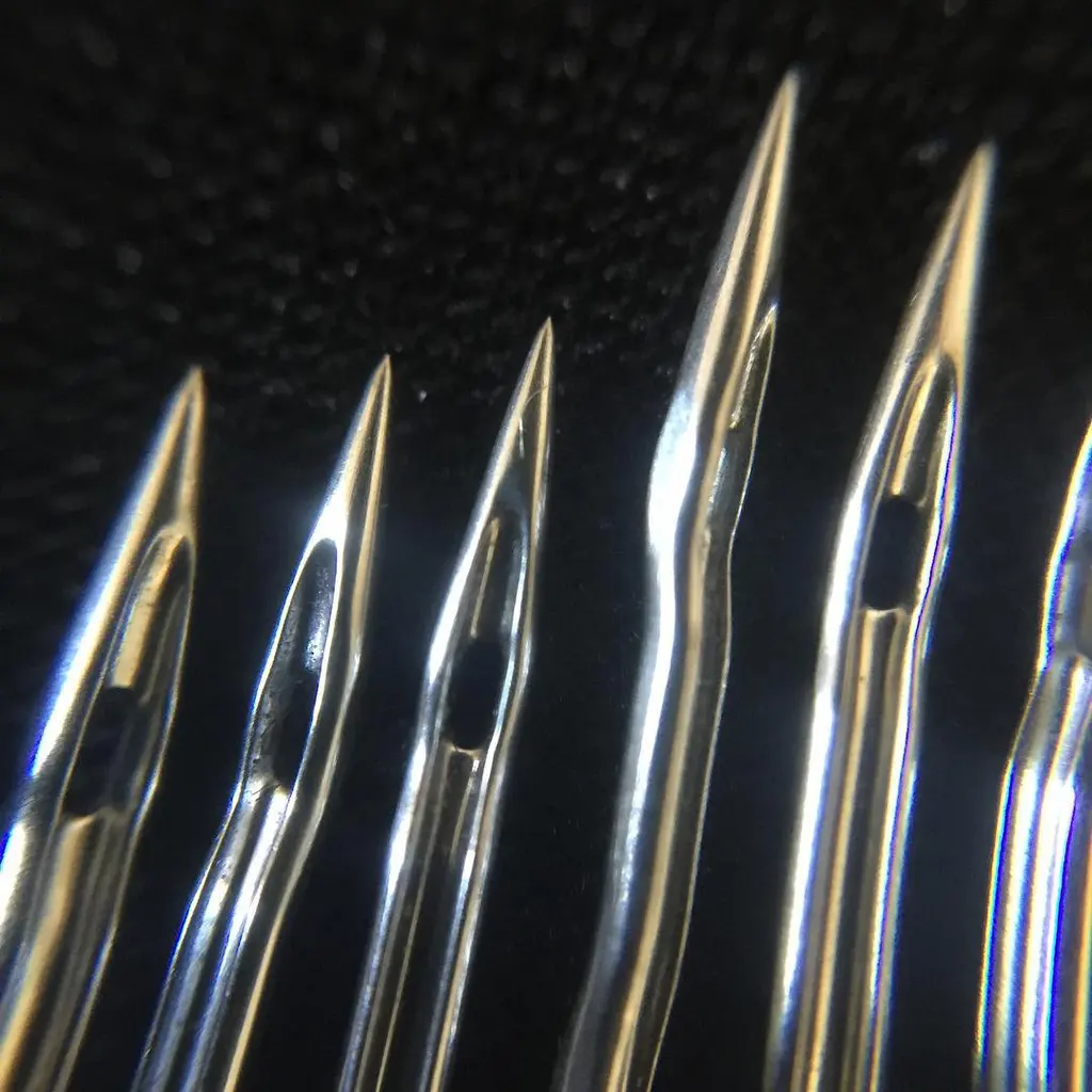 A macro photograph of sewing-machine needle tips and their eyes against a dark background.