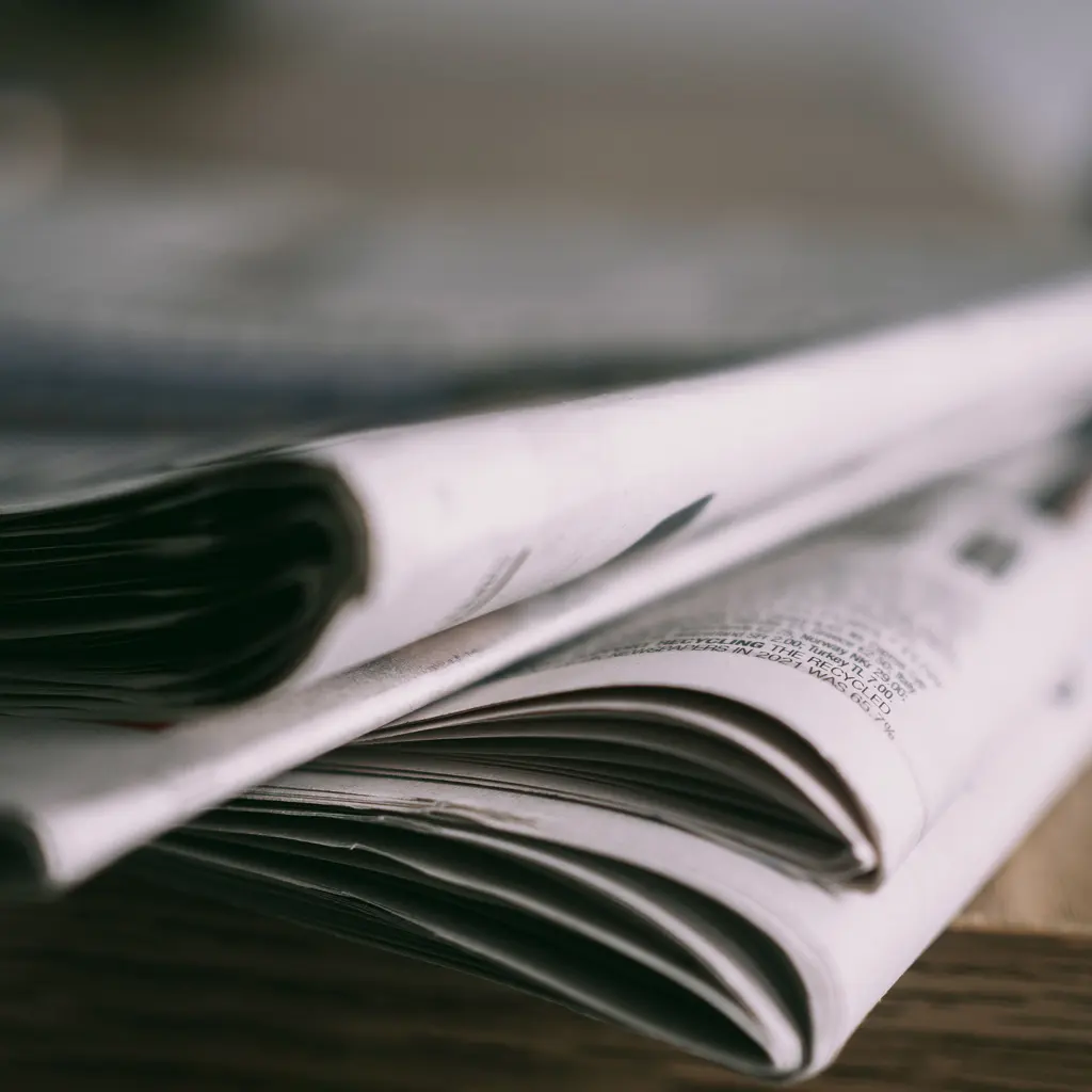 Folded newspapers showing layered pages and a rolled edge.