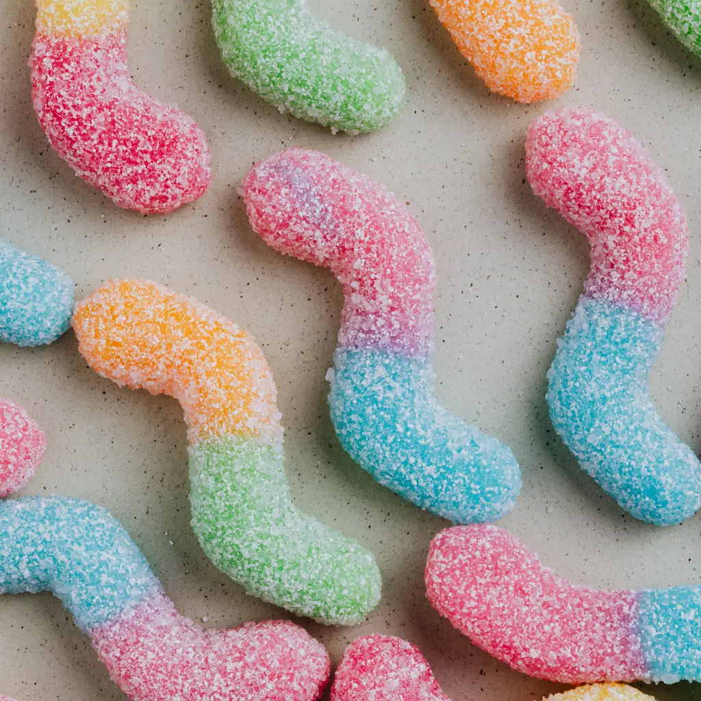 Colorful sugar-coated gummy worm candies arranged on a light surface.