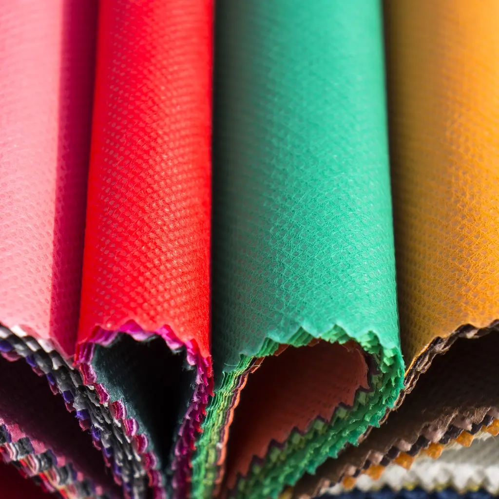 Rolls of pink, red, green and yellow nonwoven fabric with textured cut edges.