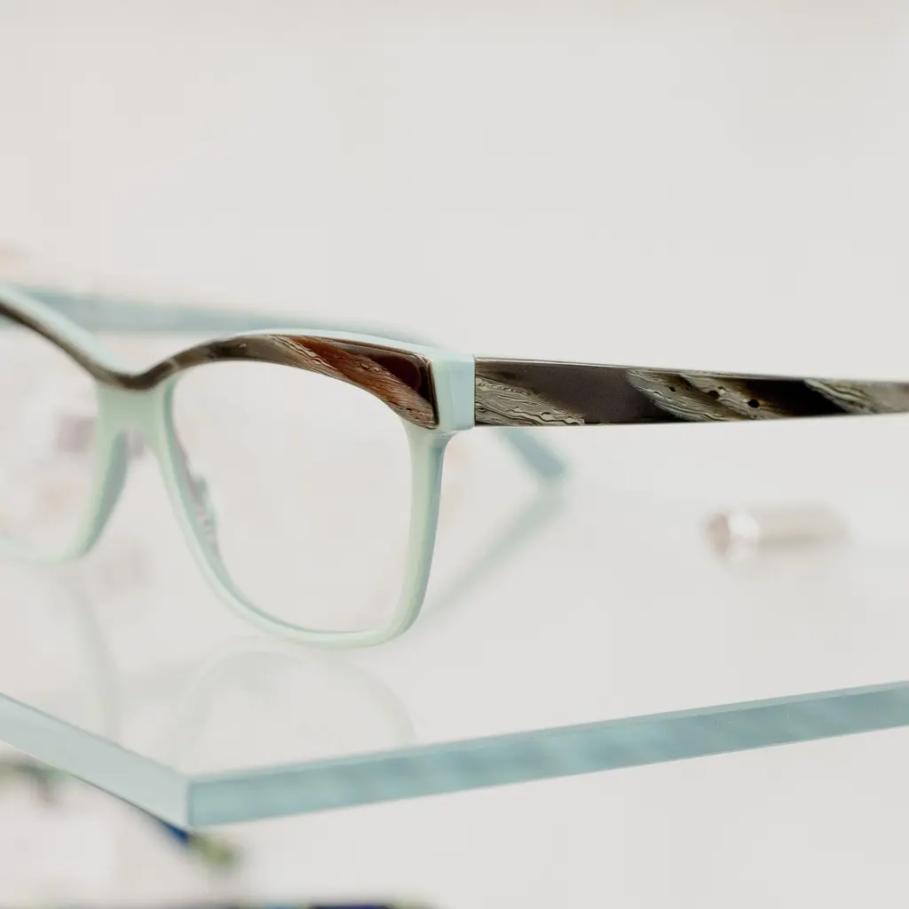 Eyeglass frames with clear lenses displayed on a glass shelf.