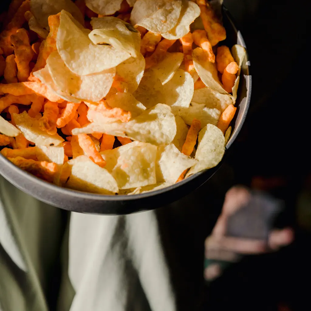 Potato chips and orange cheese snacks in a dark bowl.