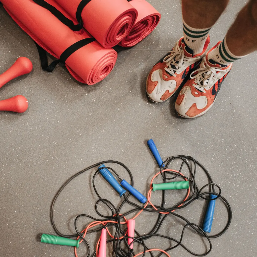 Exercise mats, small dumbbells and jump ropes arranged beside athletic shoes.