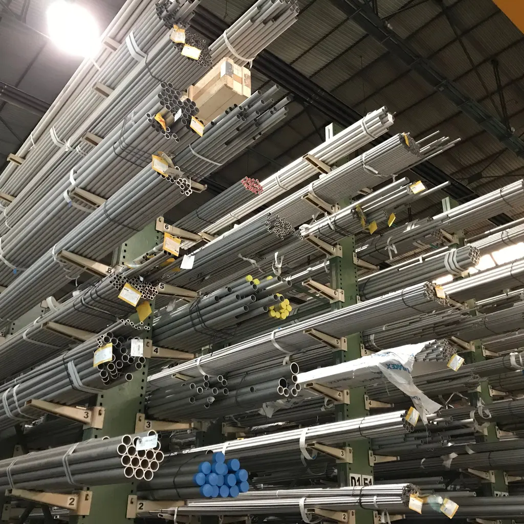 Bundles of metal tubes stored in racks inside an industrial warehouse.