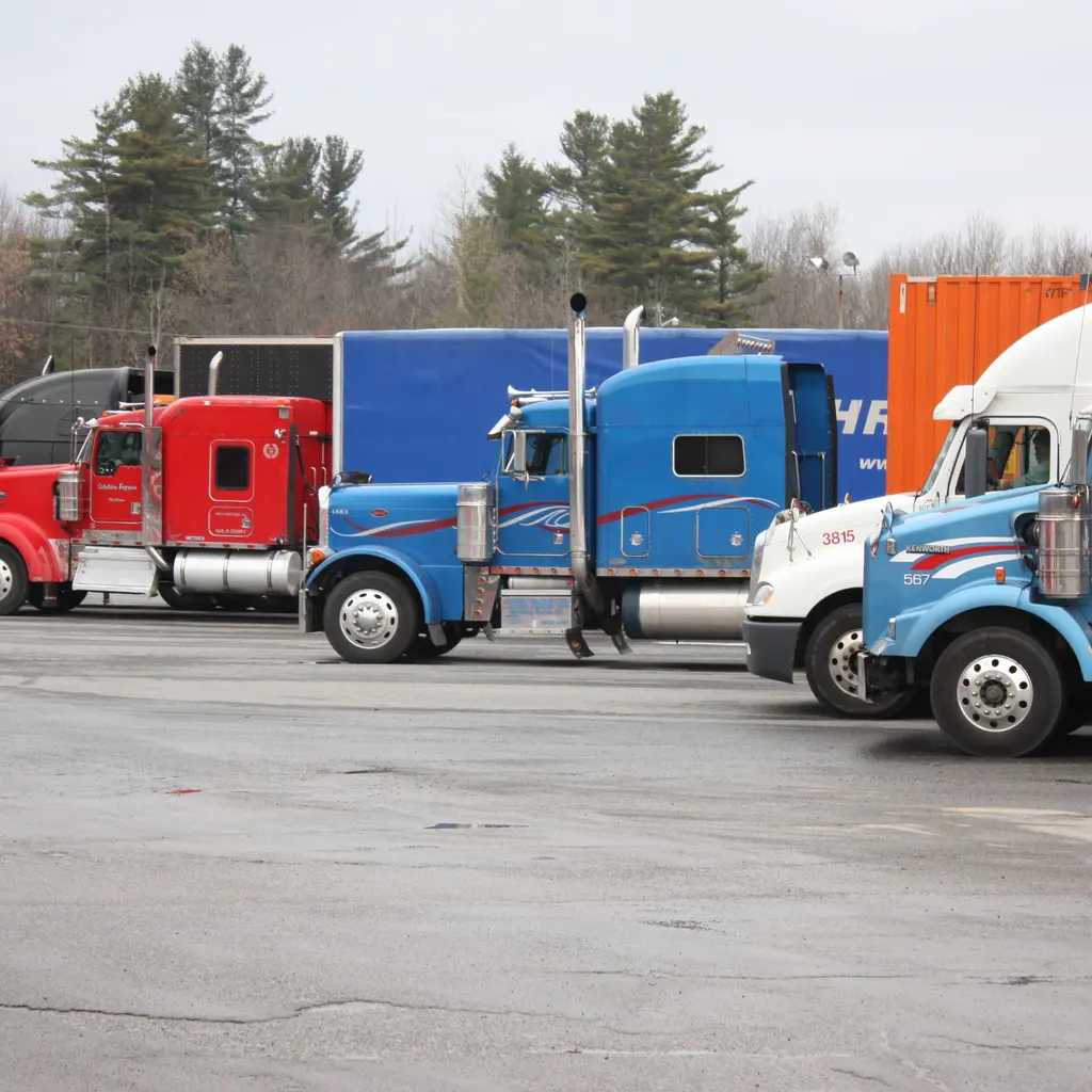 Semi-truck tractors and trailers parked in a paved lot.