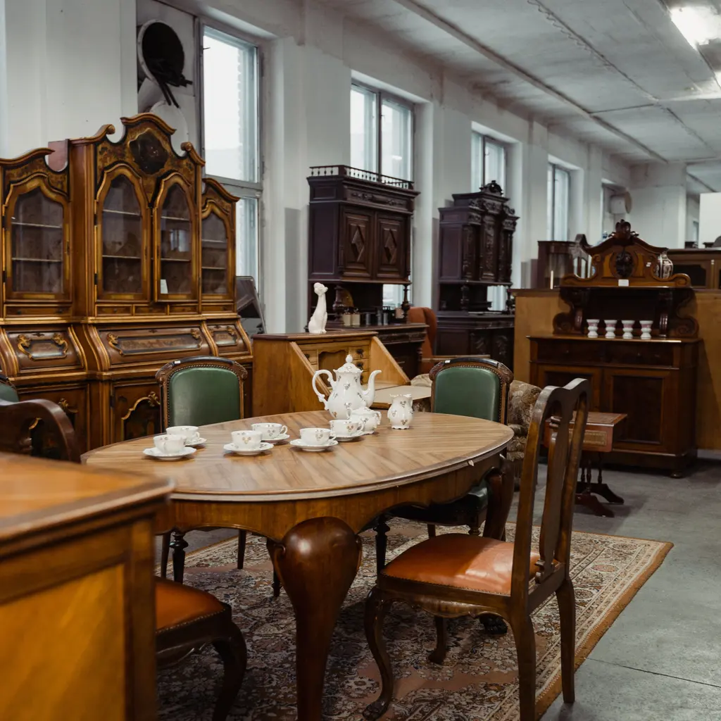Antique wooden dining furniture, display cabinets and a tea service in a showroom.