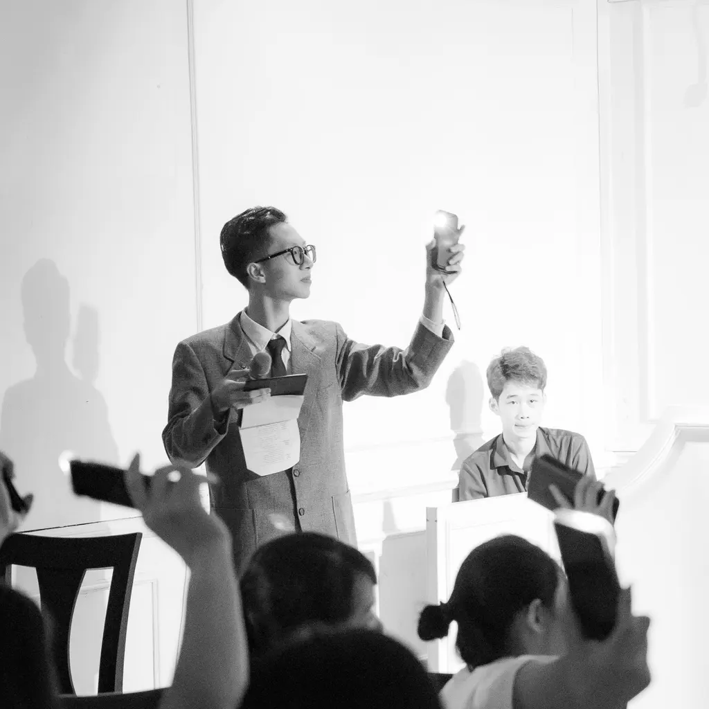 An auctioneer addressing bidders holding numbered paddles and phones in a sale room.
