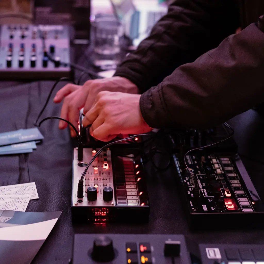 Hands connecting cables to tabletop audio mixers and sound-processing equipment.