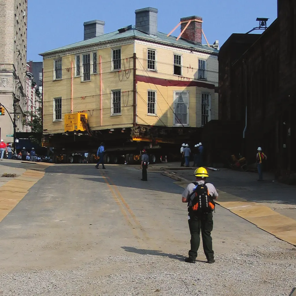 A historic house raised on hydraulic dollies for relocation along a street.