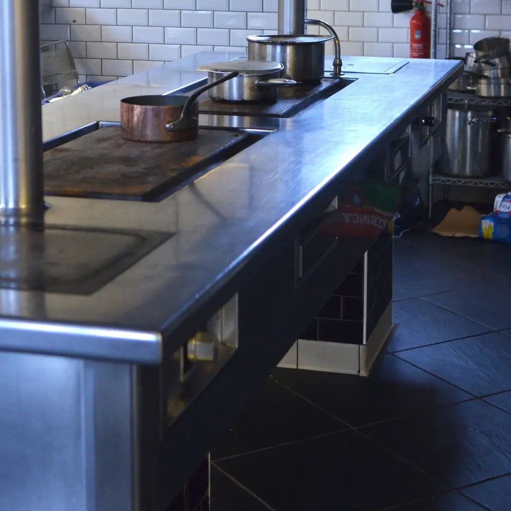 A stainless-steel commercial cooking range with cooking pots and a continuous work surface.