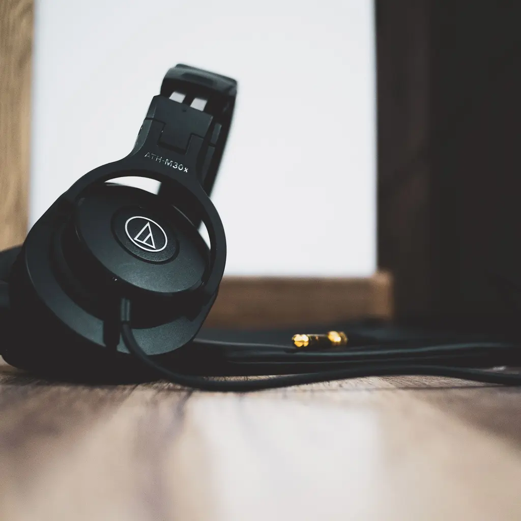 Black wired over-ear headphones with their audio cable and plug resting on a wooden surface.