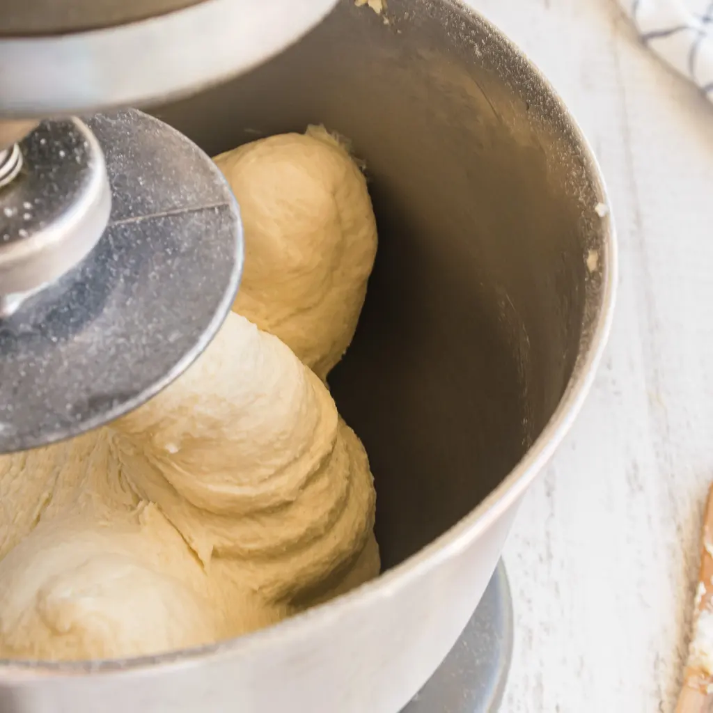 Pale dough being kneaded inside a stainless-steel mixer bowl.
