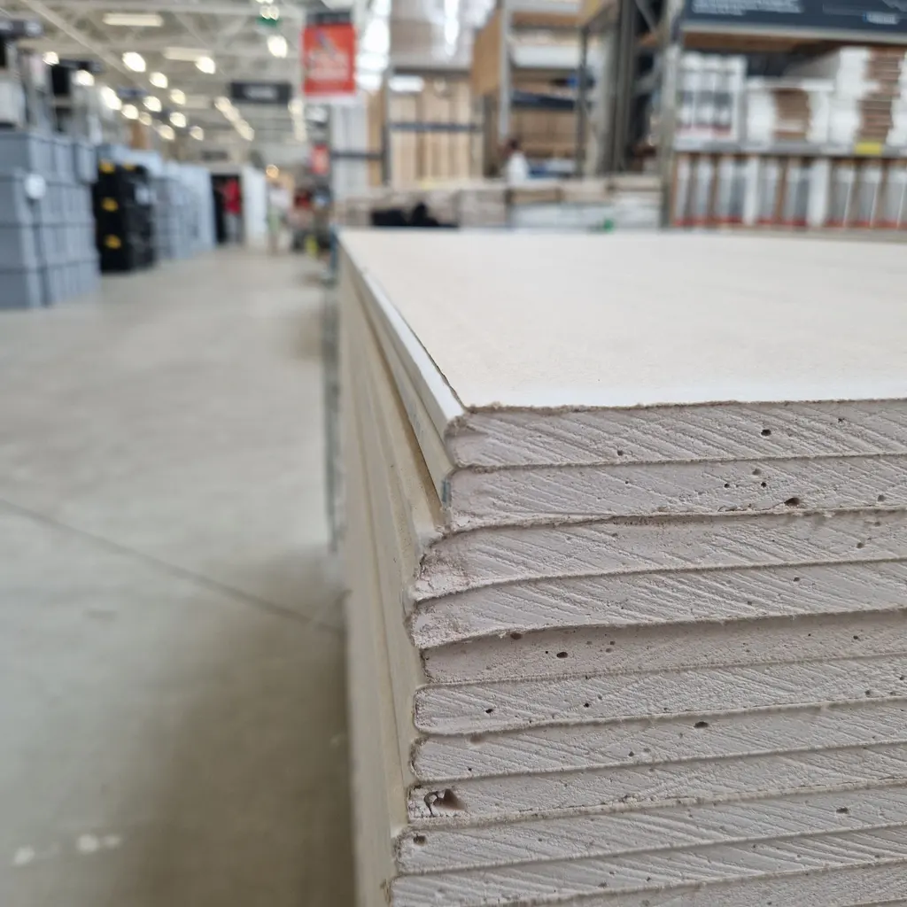 Stacked gypsum drywall boards showing their white faces and layered cut edges in a warehouse.