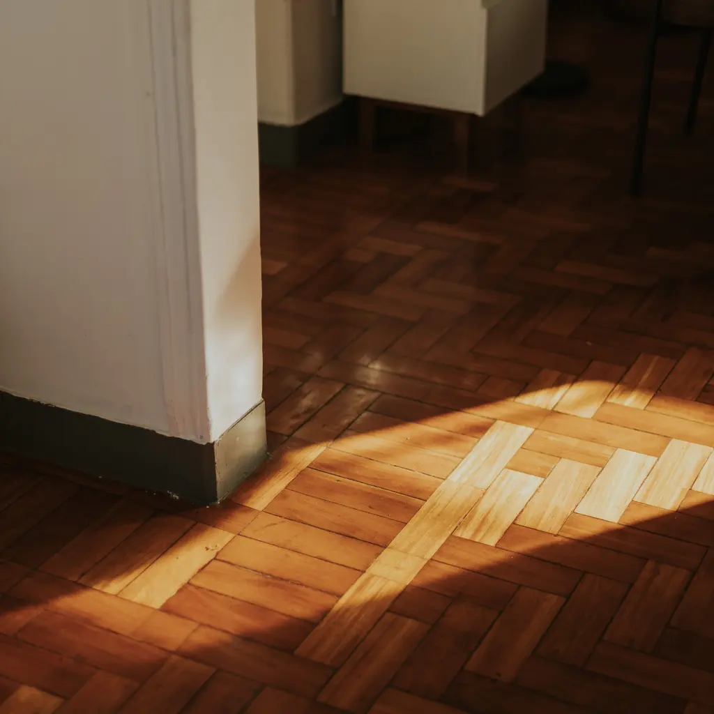 Sunlight across a finished wood parquet floor beside an interior doorway.