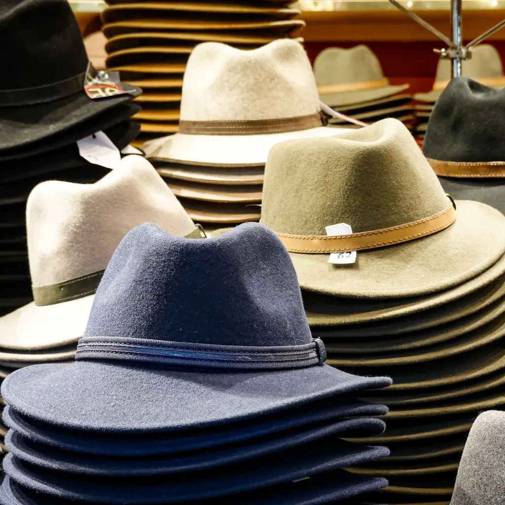 Stacks of felt fedora hats in cream, green and dark blue on a display counter.